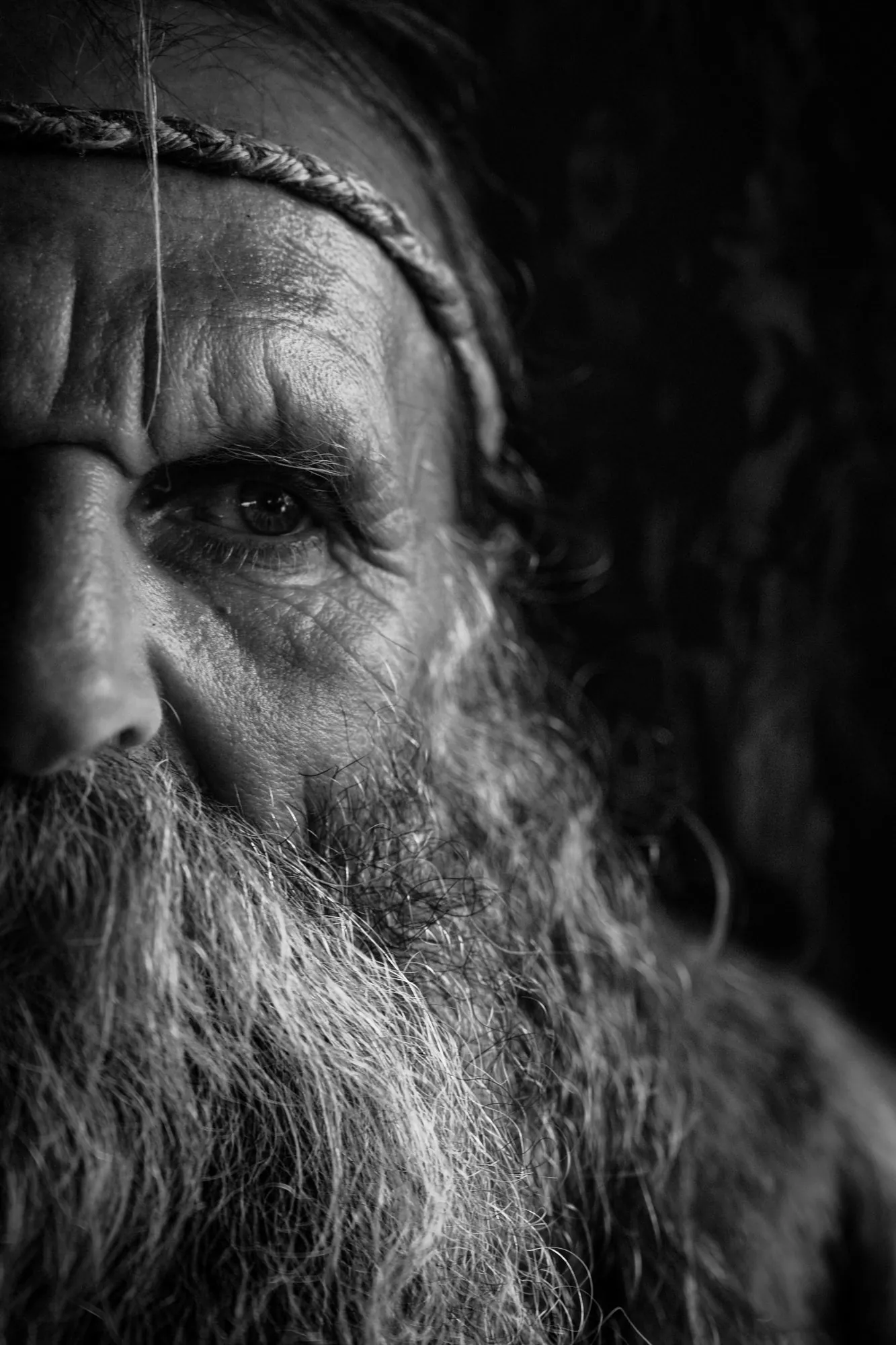 Close black-and-white portrait of a bearded man wearing a braided headband