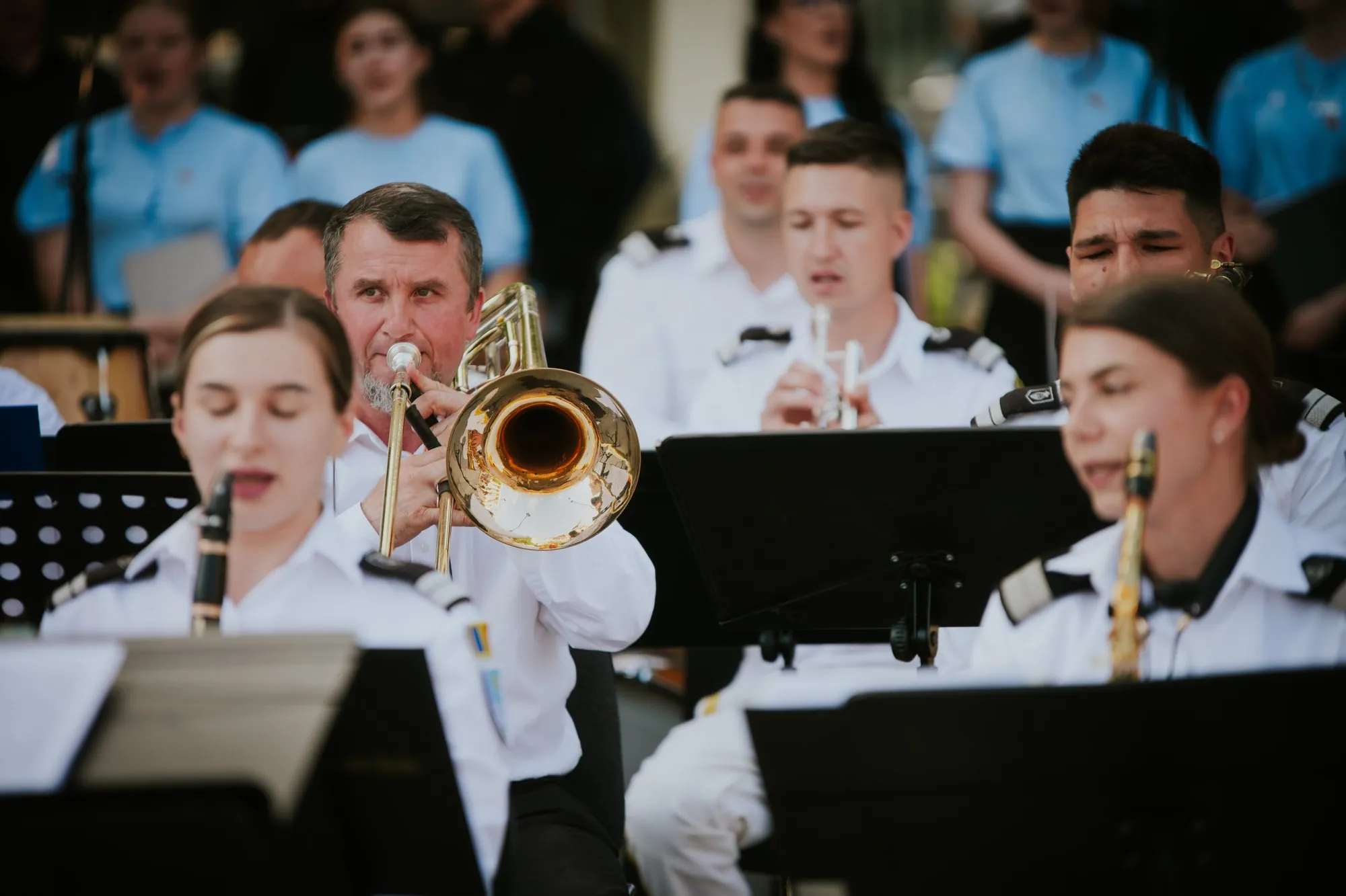 Military band musician playing trombone with a choir behind him