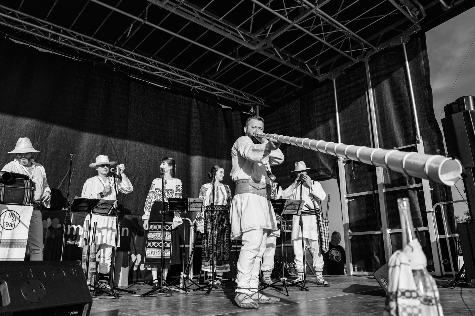 Black-and-white stage view with a musician sending the line of a long wooden horn toward the audience.