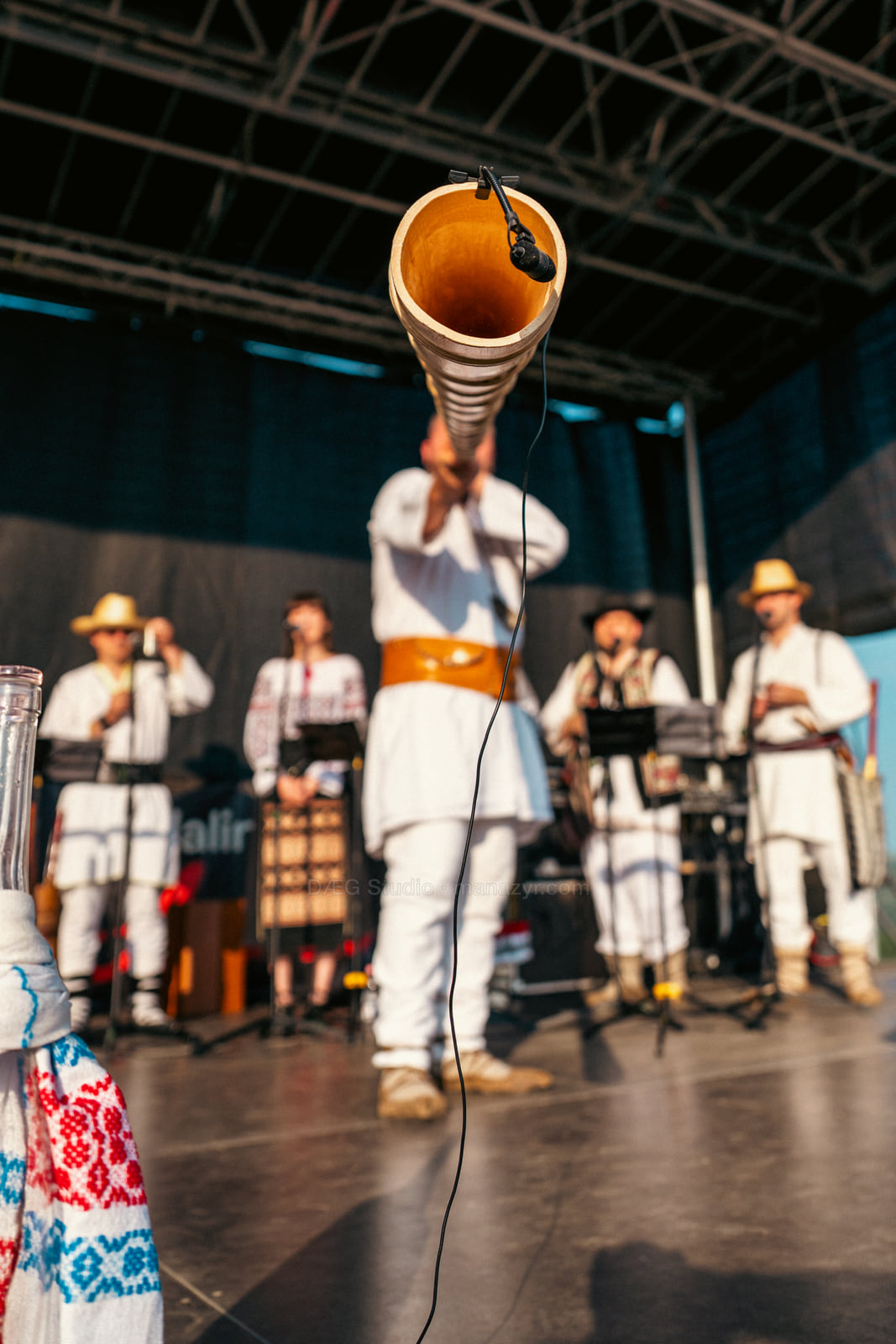 Close view into the bell of a wooden horn with the folk ensemble softly blurred behind it.