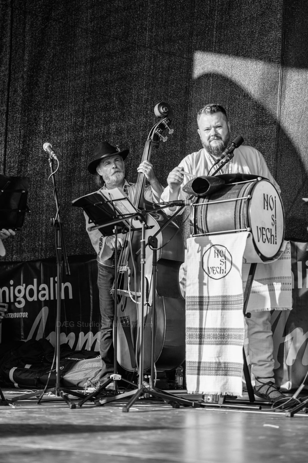 Black-and-white portrait of a drummer and an older double bassist sharing the stage.