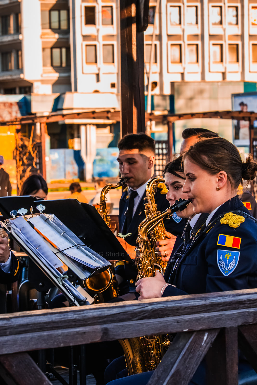 Uniformed saxophonist performs beside music stands in warm evening light.