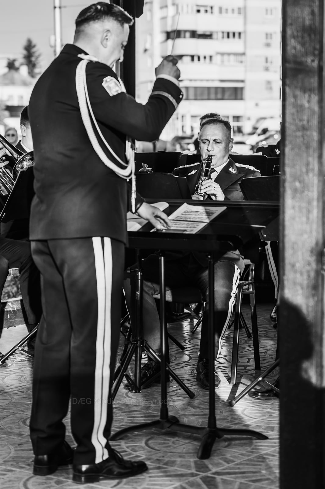 Black-and-white view of the conductor leading musicians beneath the pavilion.