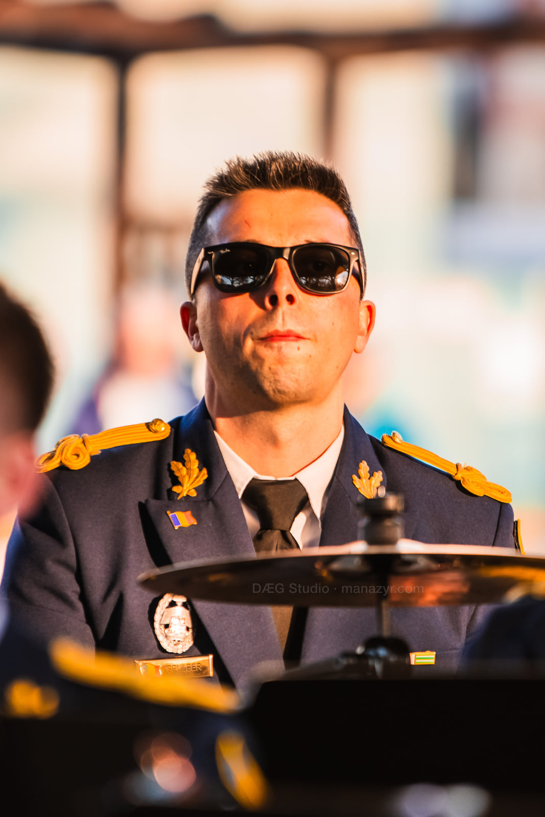 Percussionist in dark ceremonial uniform performs under warm pavilion light.