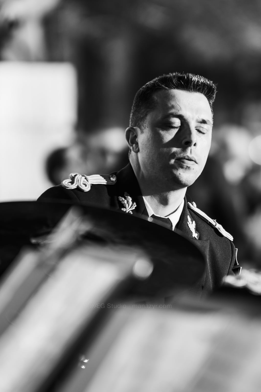 Black-and-white portrait of a focused band musician performing behind blurred music stands.
