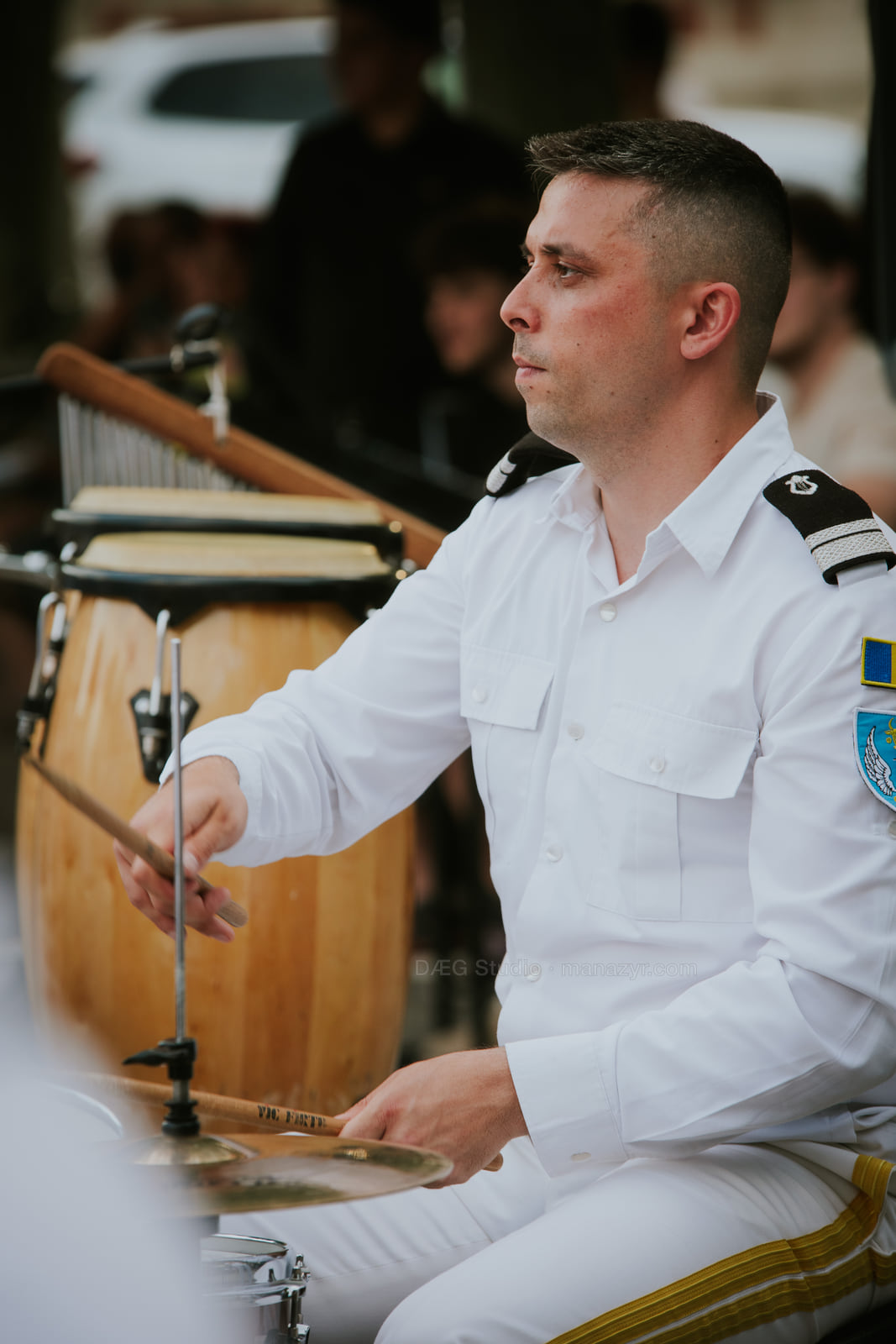 Drummer in a white ceremonial uniform plays with a focused expression.