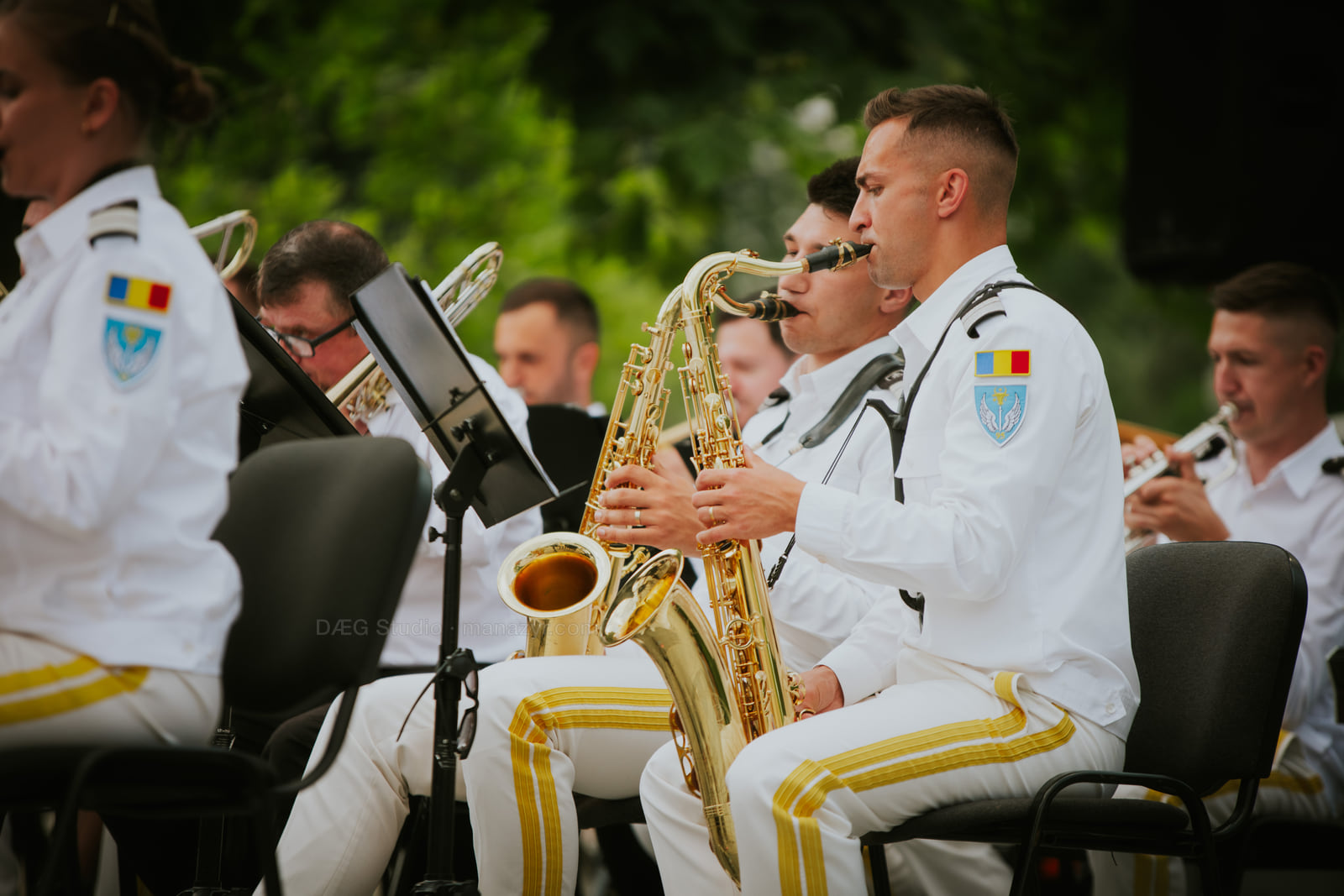 Seated saxophonists in white uniforms perform together during an outdoor concert.