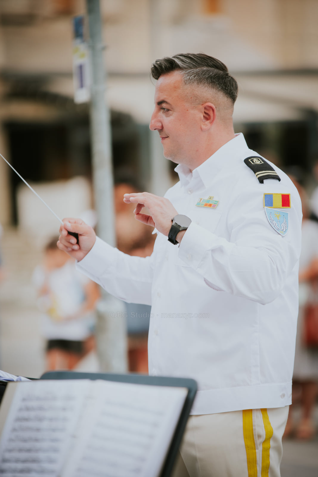 Conductor in a white uniform leads the ensemble with a raised baton.