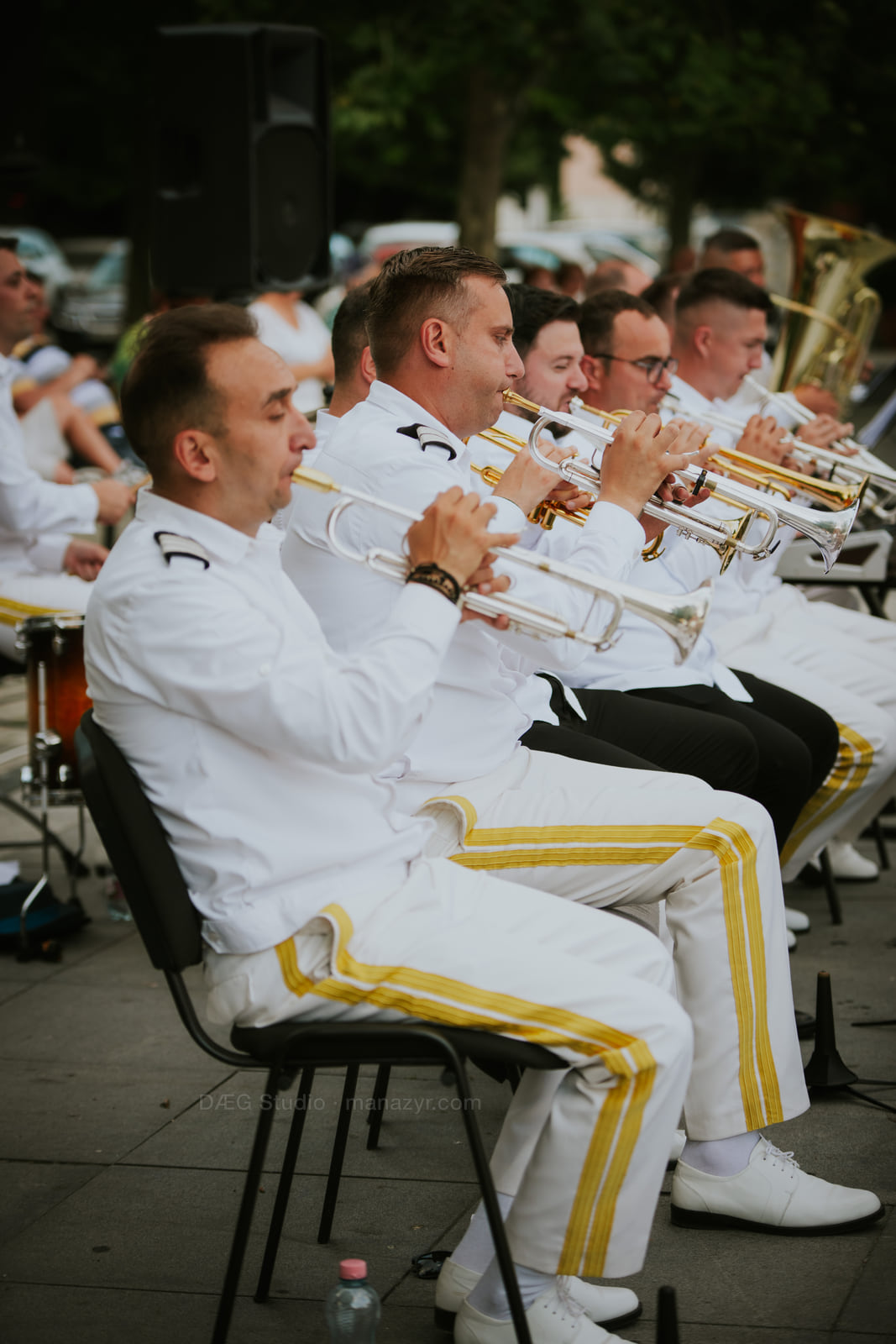 Trumpet players in white uniforms perform in a synchronized seated row.