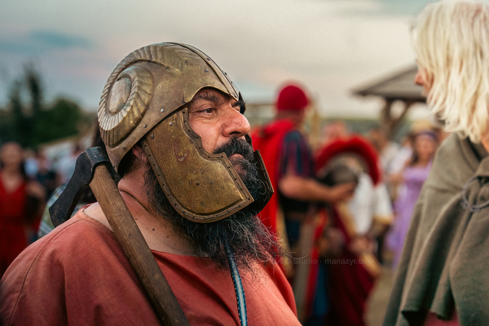 Side portrait of a bearded reenactor in a weathered bronze-colored helmet.