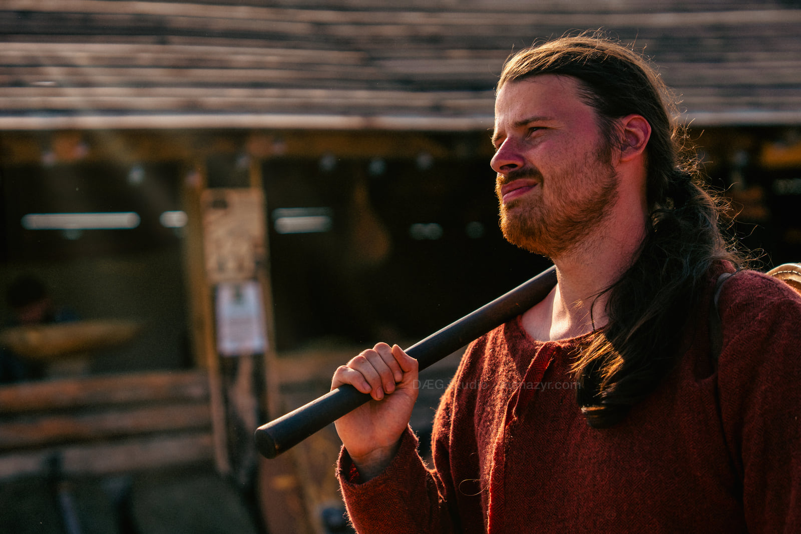 Reenactor in a red tunic carries a long-handled axe across his shoulder.