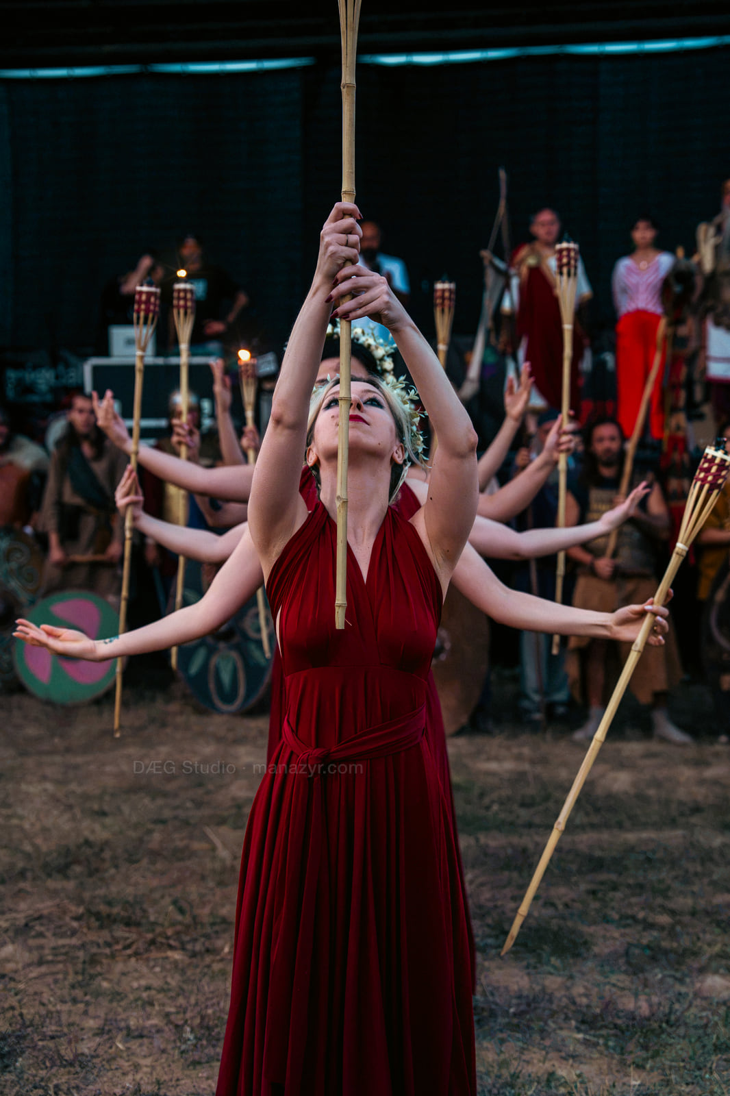 Performer in a red dress raises a staff as dancers form radiating arms behind her.
