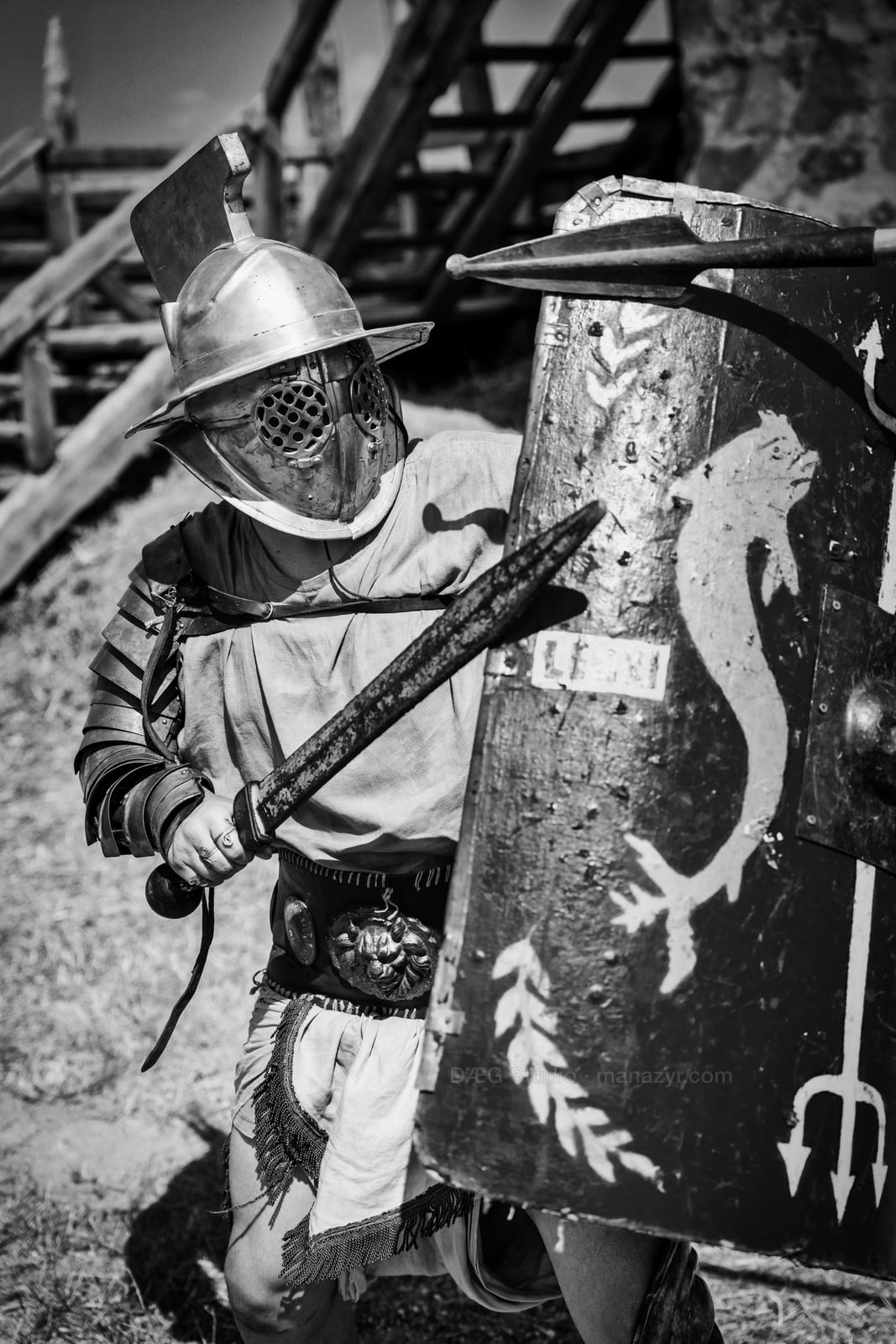 Black-and-white portrait of an armored reenactor holding a sword behind a weathered shield.