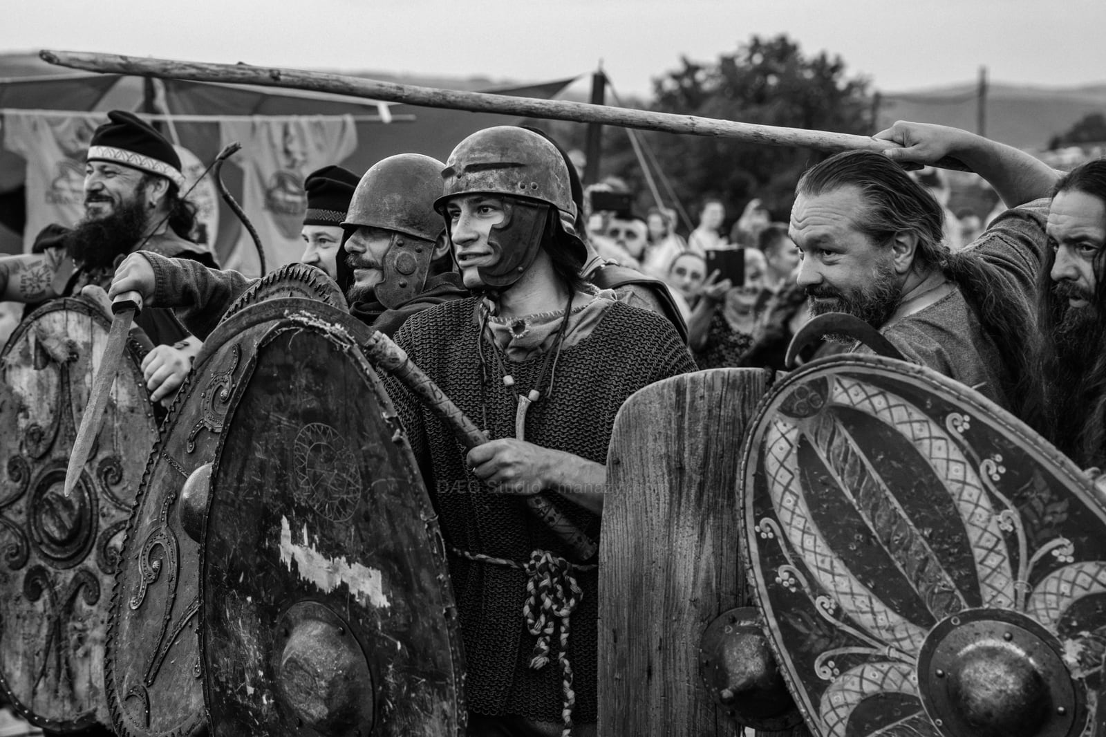Black-and-white group of reenactors standing shoulder to shoulder with painted wooden shields.