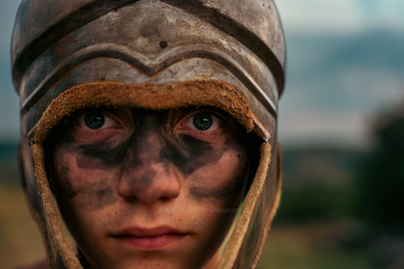 Close portrait of a helmeted young performer with dark ceremonial paint across the face.