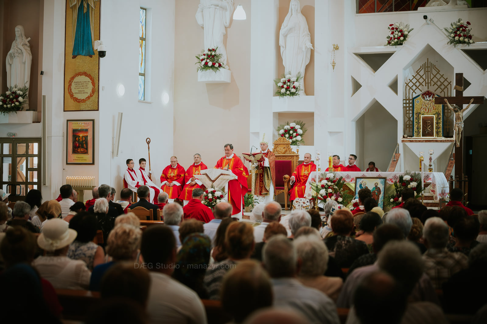 Vedere amplă a credincioșilor adunați în fața clericilor în veșminte roșii, la altar.