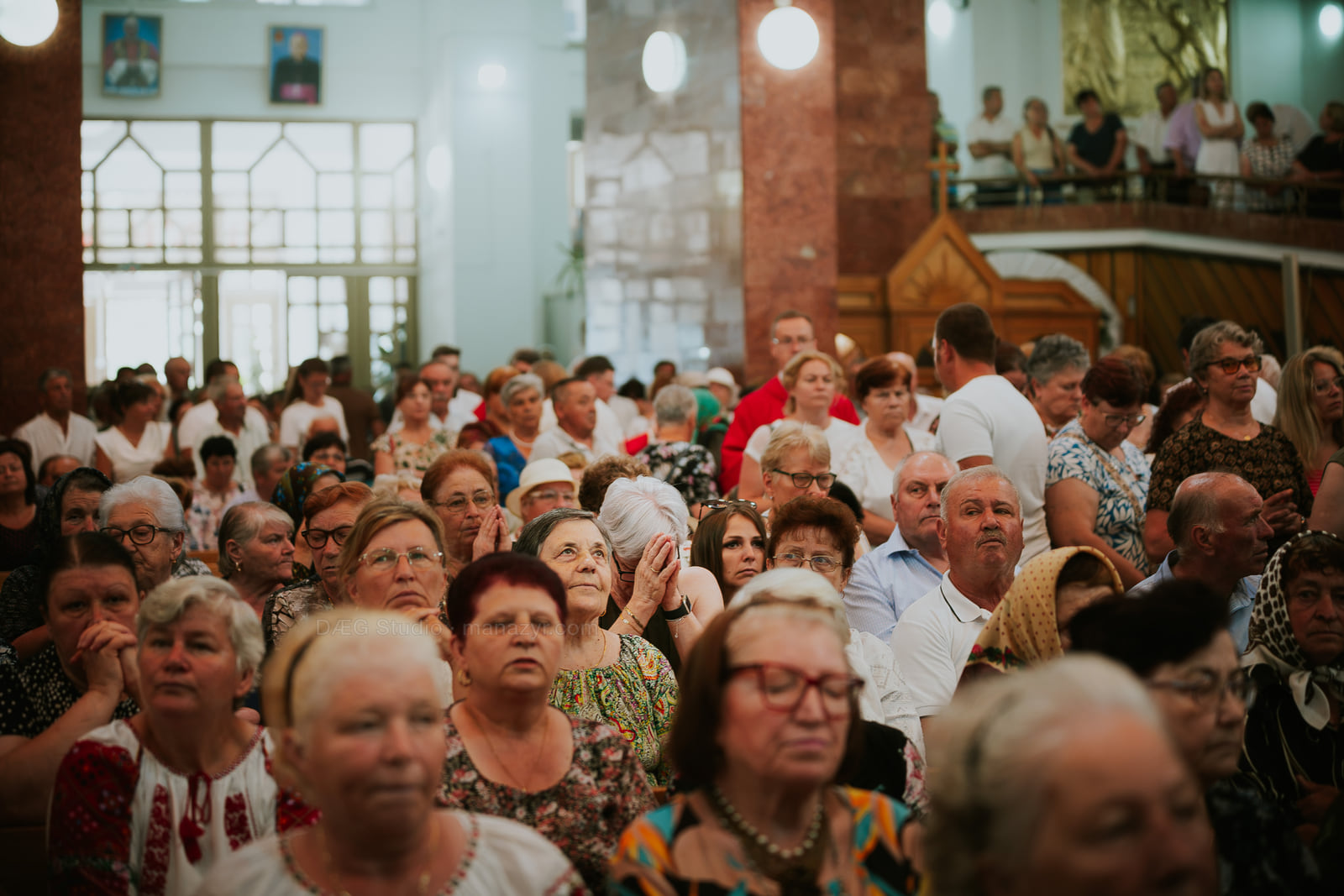 Mulțimea urmărește slujba, iar mai mulți credincioși își împreunează mâinile în rugăciune.