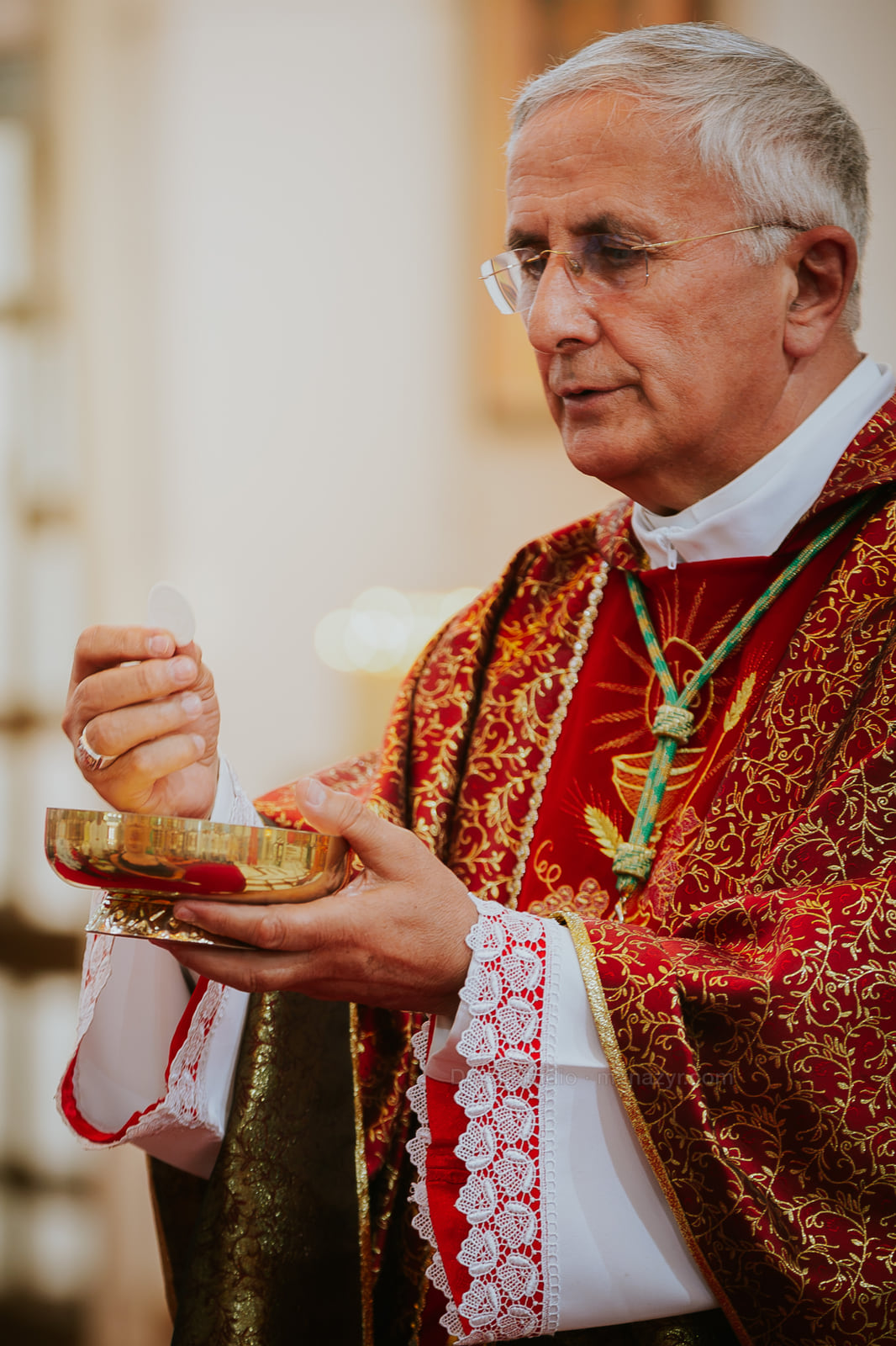Episcopul ține ostia deasupra unui potir auriu în timpul slujbei.