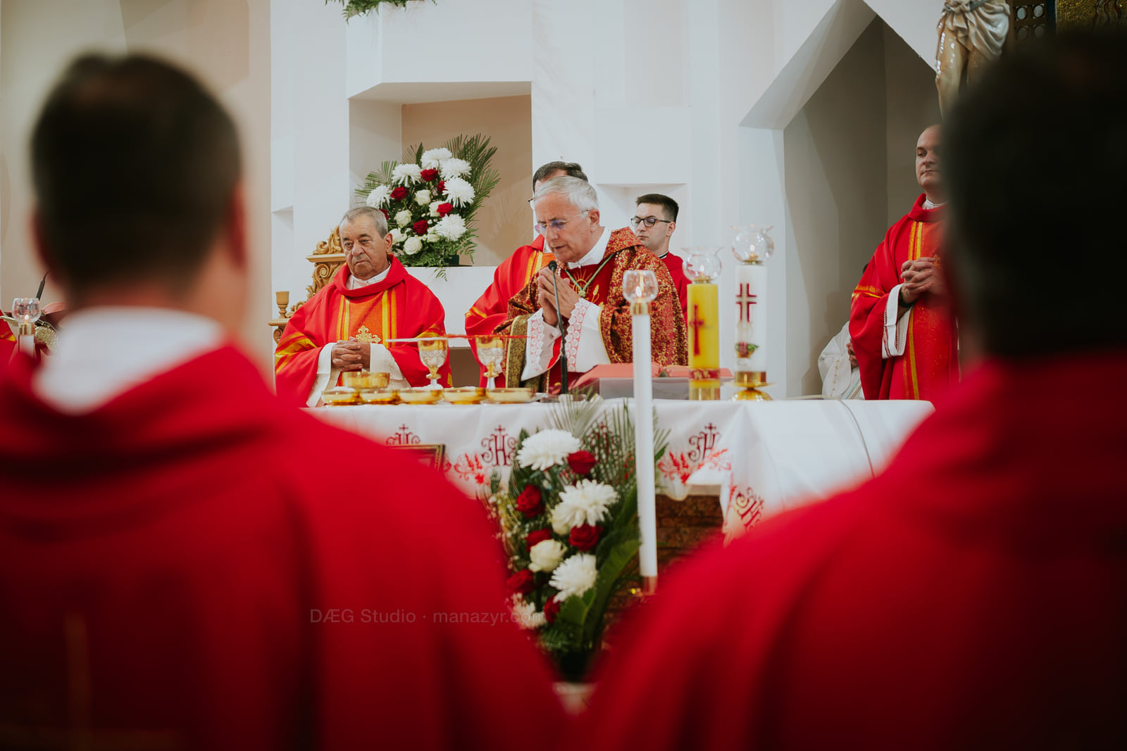 Episcopul la altar este încadrat de veșmintele roșii ale clericilor din apropiere.