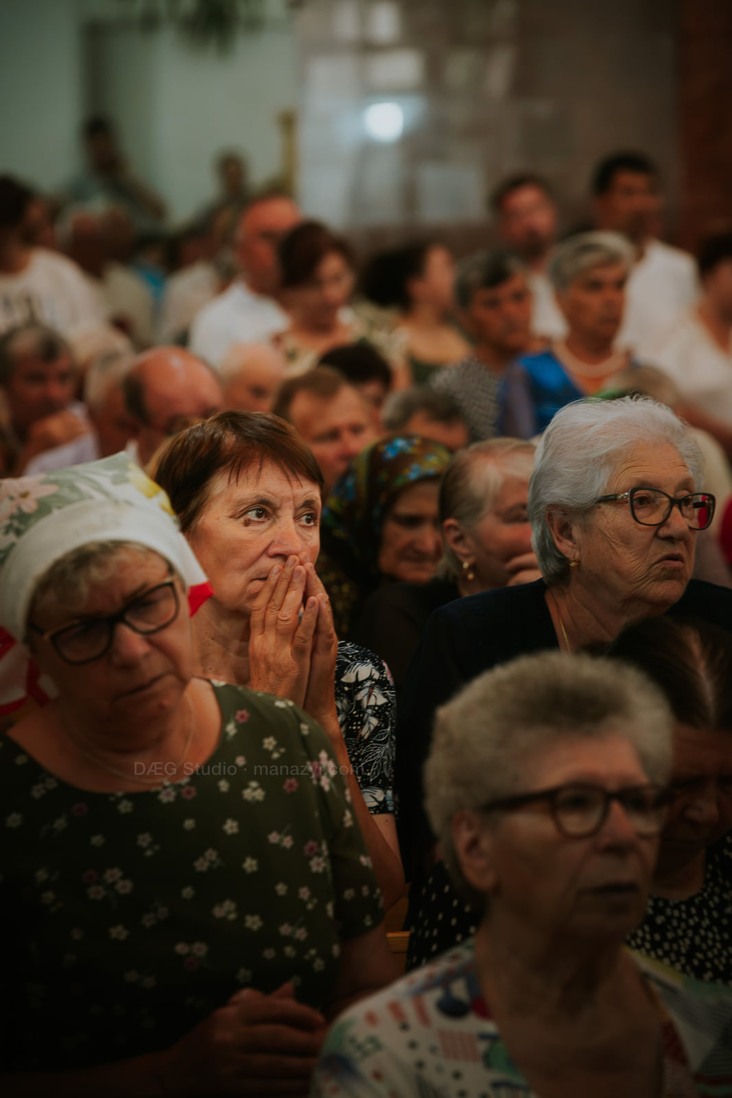 Femeile din mulțime privesc în liniște, una ținând mâinile împreunate lângă chip.