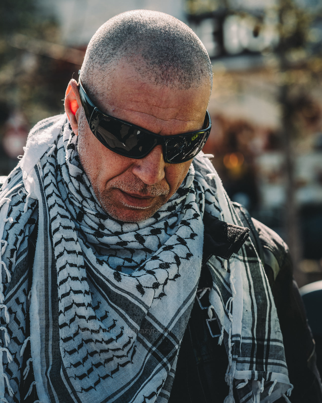 Close portrait of a man in dark sunglasses and a patterned black-and-white scarf.