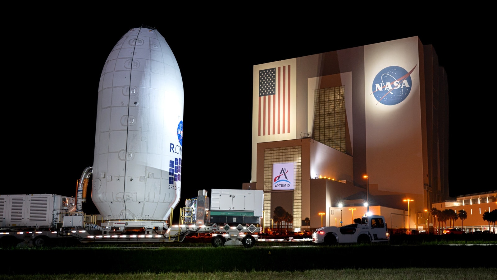 The encapsulated Nancy Grace Roman Space Telescope moving at night toward SpaceX's hangar at Kennedy Space Center